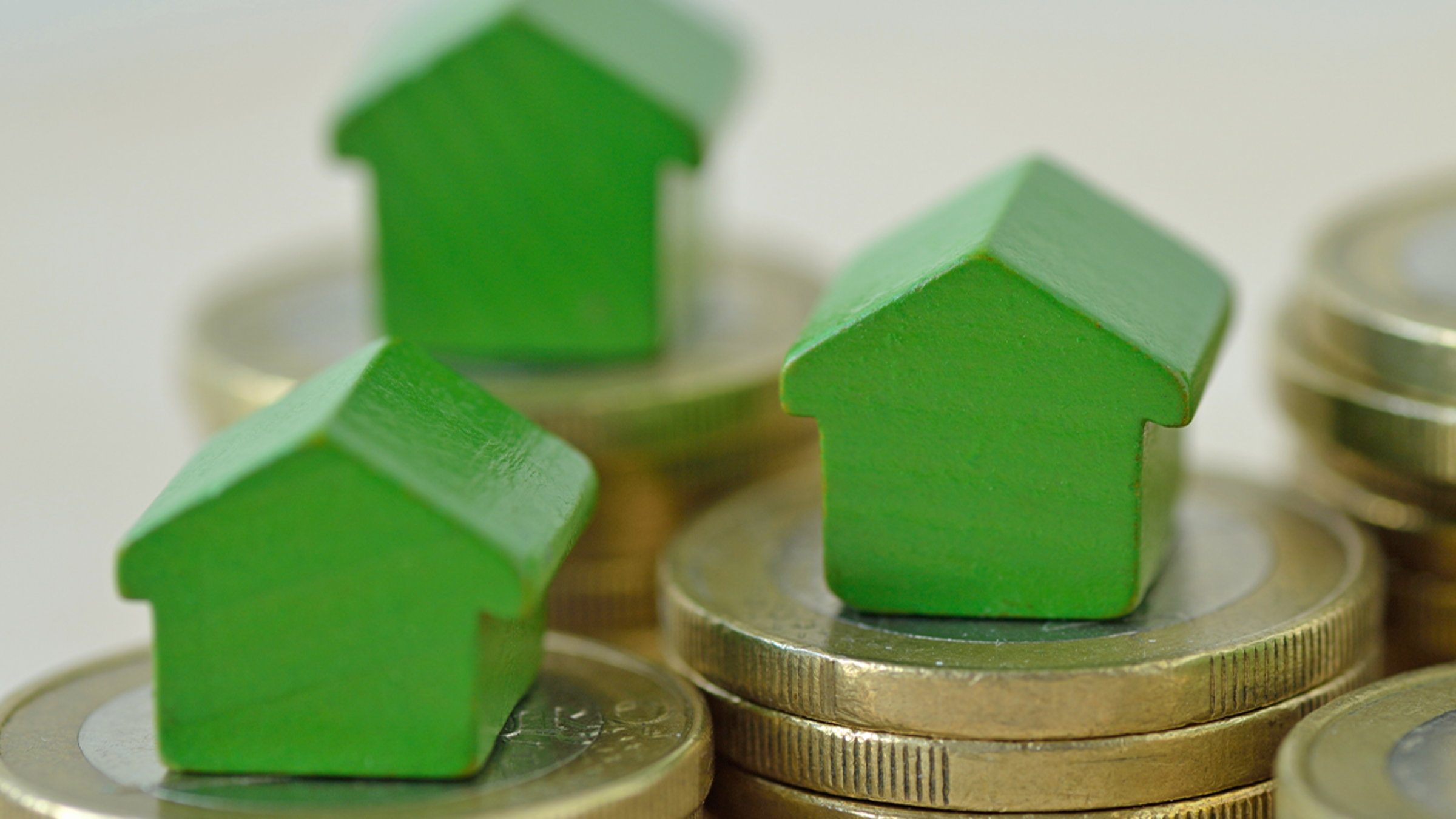Three miniature houses sit atop stacks of coins