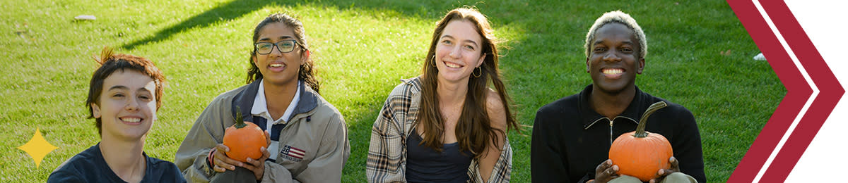 Group of four students smile holding pumpkins