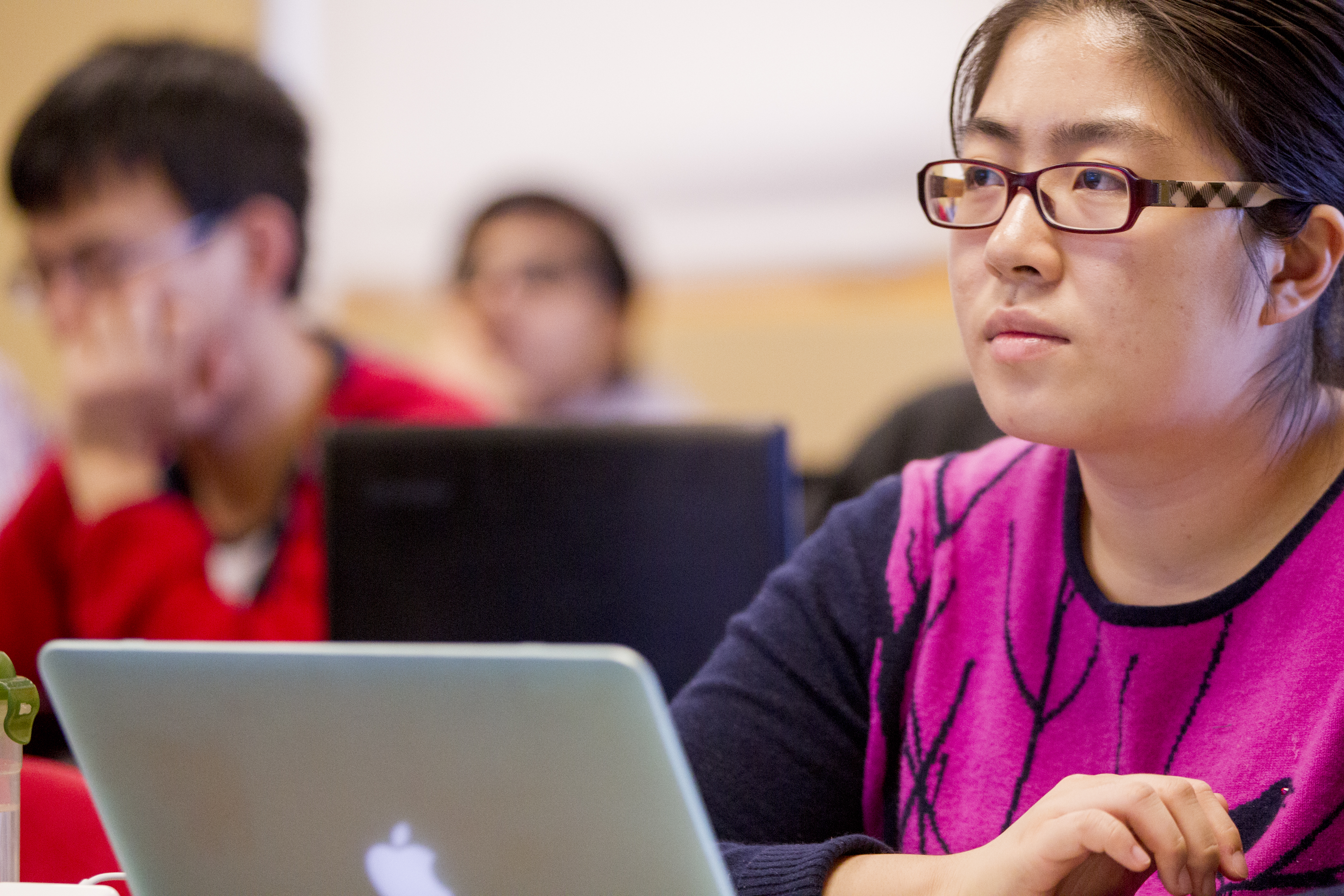 A student with her laptop looks ahead toward lecturing professor