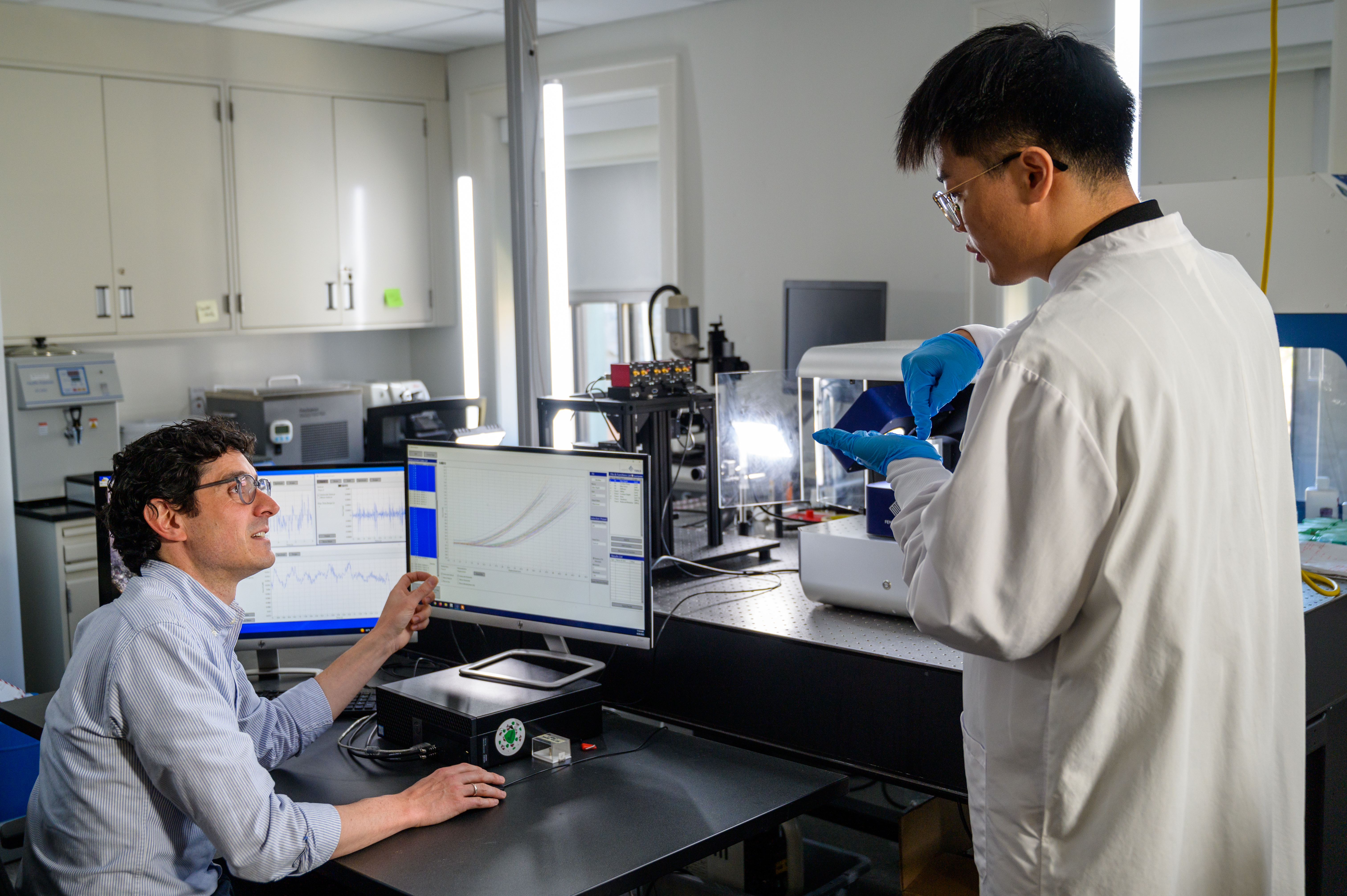 Professor in lab gestures to information on monitor while student looks on.