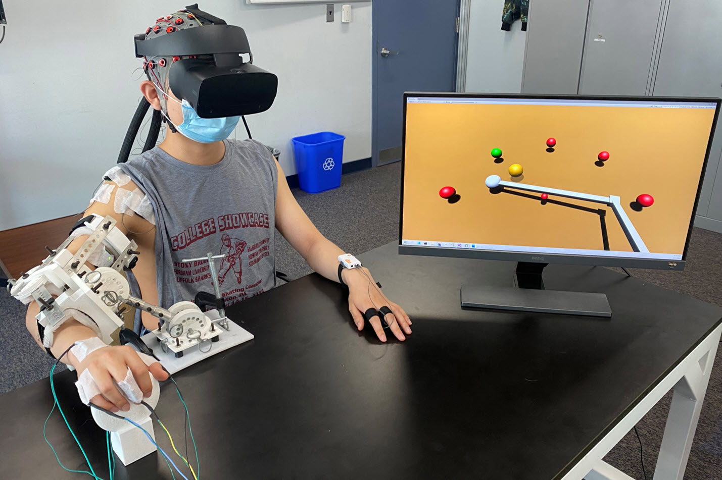 A person wearing a VR headset and arm brace equipped with sensors plays a computer game to improve coordination, strength and muscle control