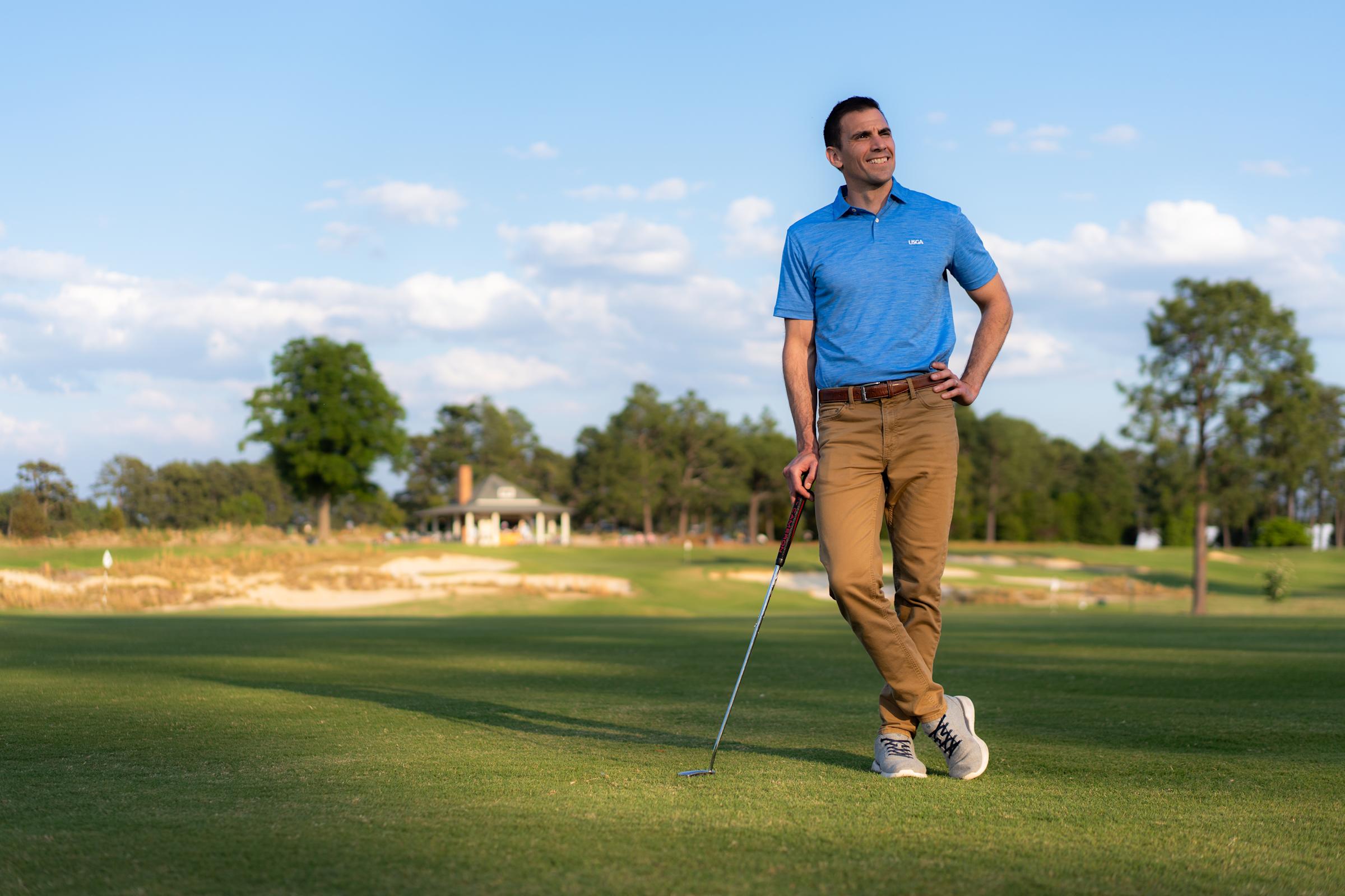 Anthony Santora M.S. ’05 portrait in blue USGA shirt leaning on golf club at golf course