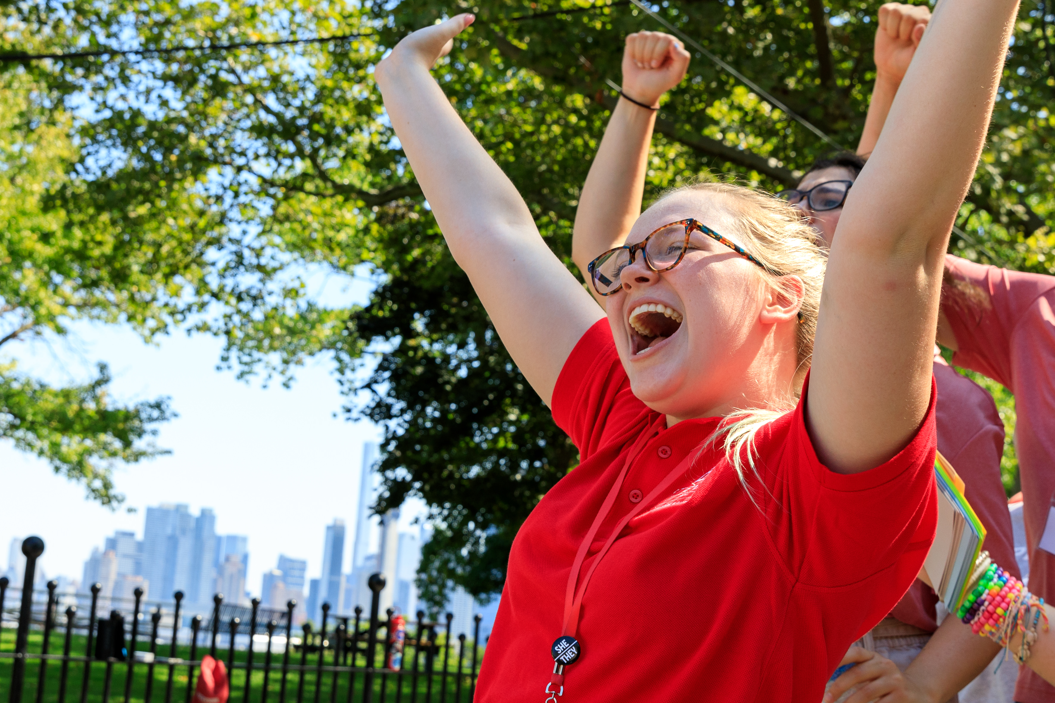 A female student in a red shirt throws her hands in the air, smiling.