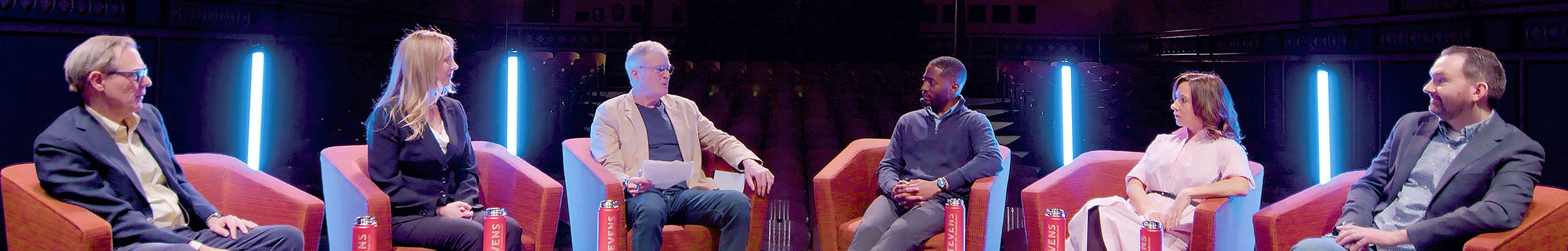 Six Stevens professors sit in chairs in conversation.