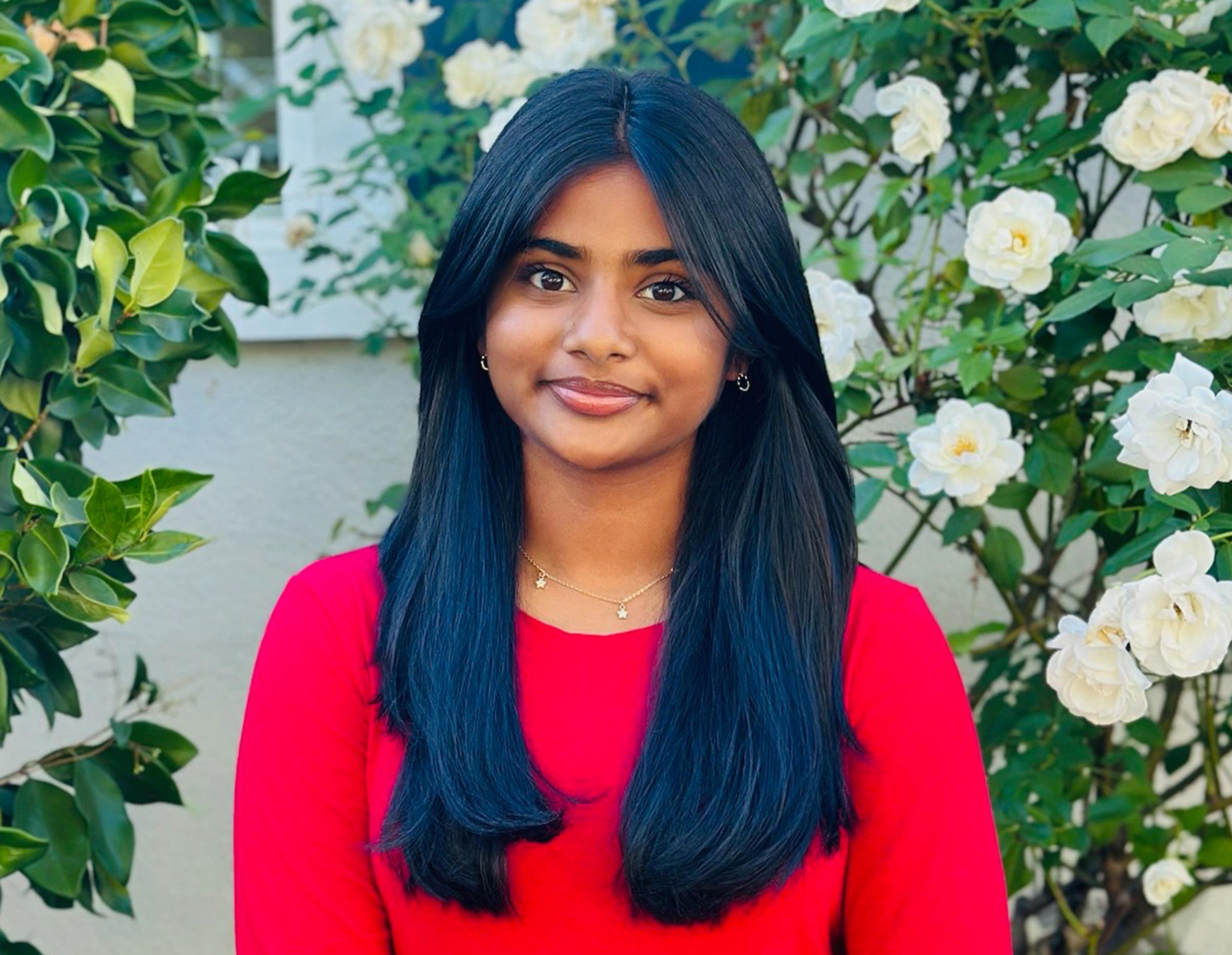 Girl in a red sweater stands in a garden.