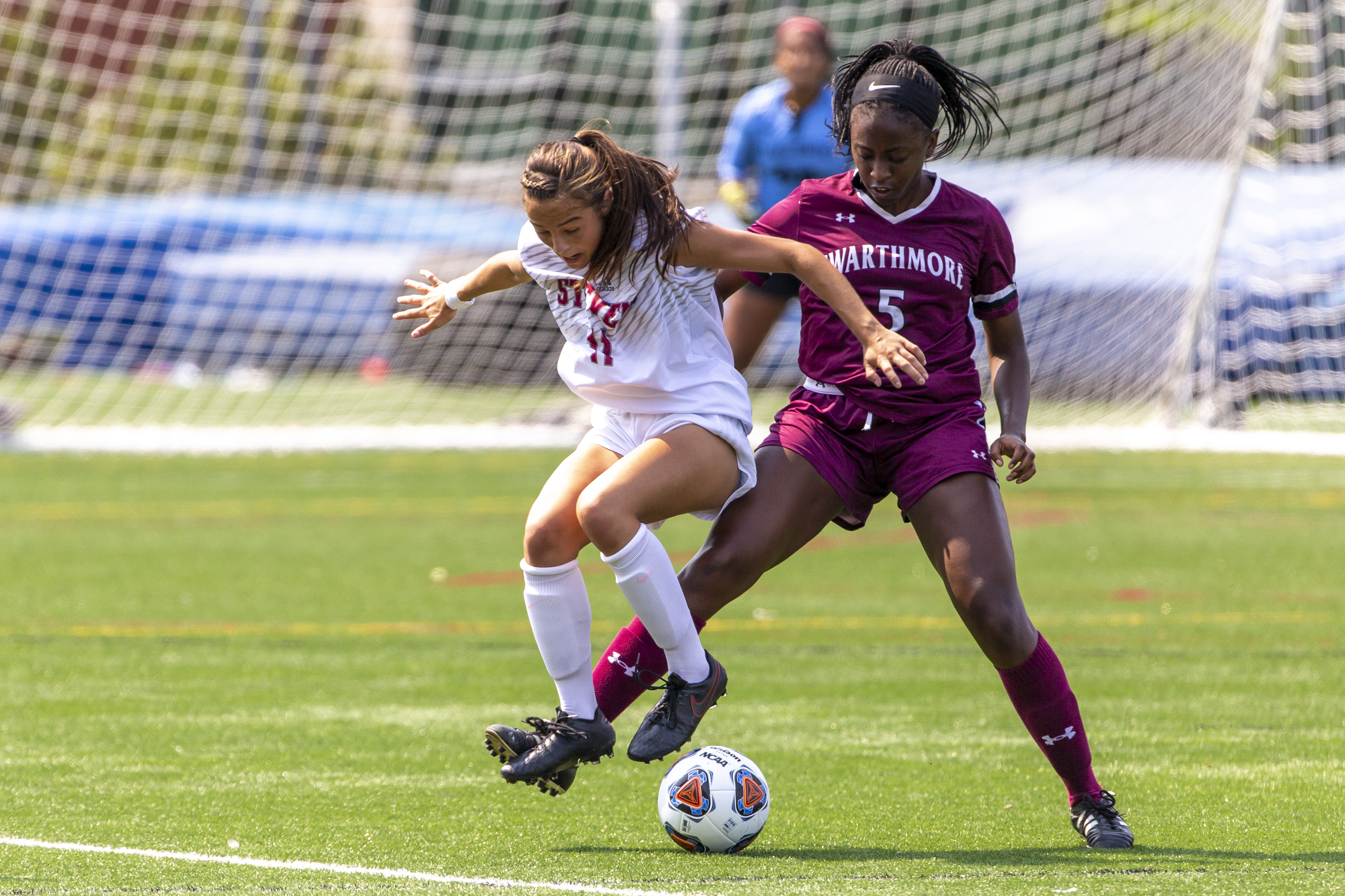 Jenna Mucci jumping to kick a soccer ball, leading over a woman from the competing team
