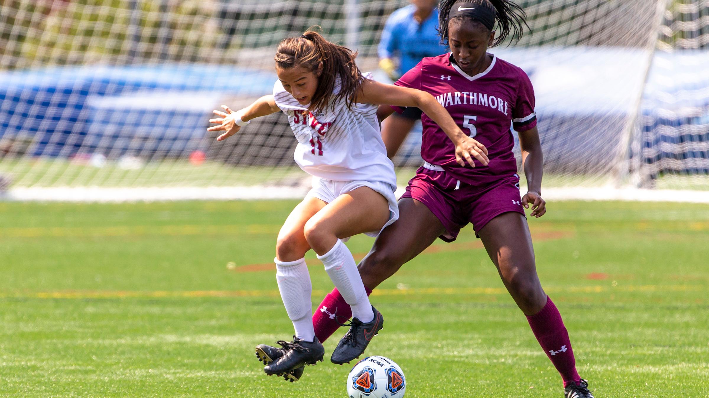 Jenna Mucci jumping to kick a soccer ball, leading over a woman from the competing team
