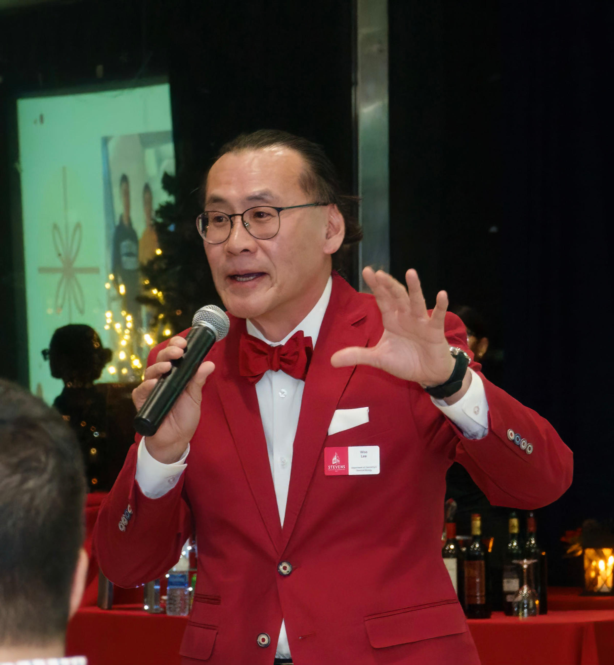 Photo of Woo Lee in a red suit speaking into a microphone