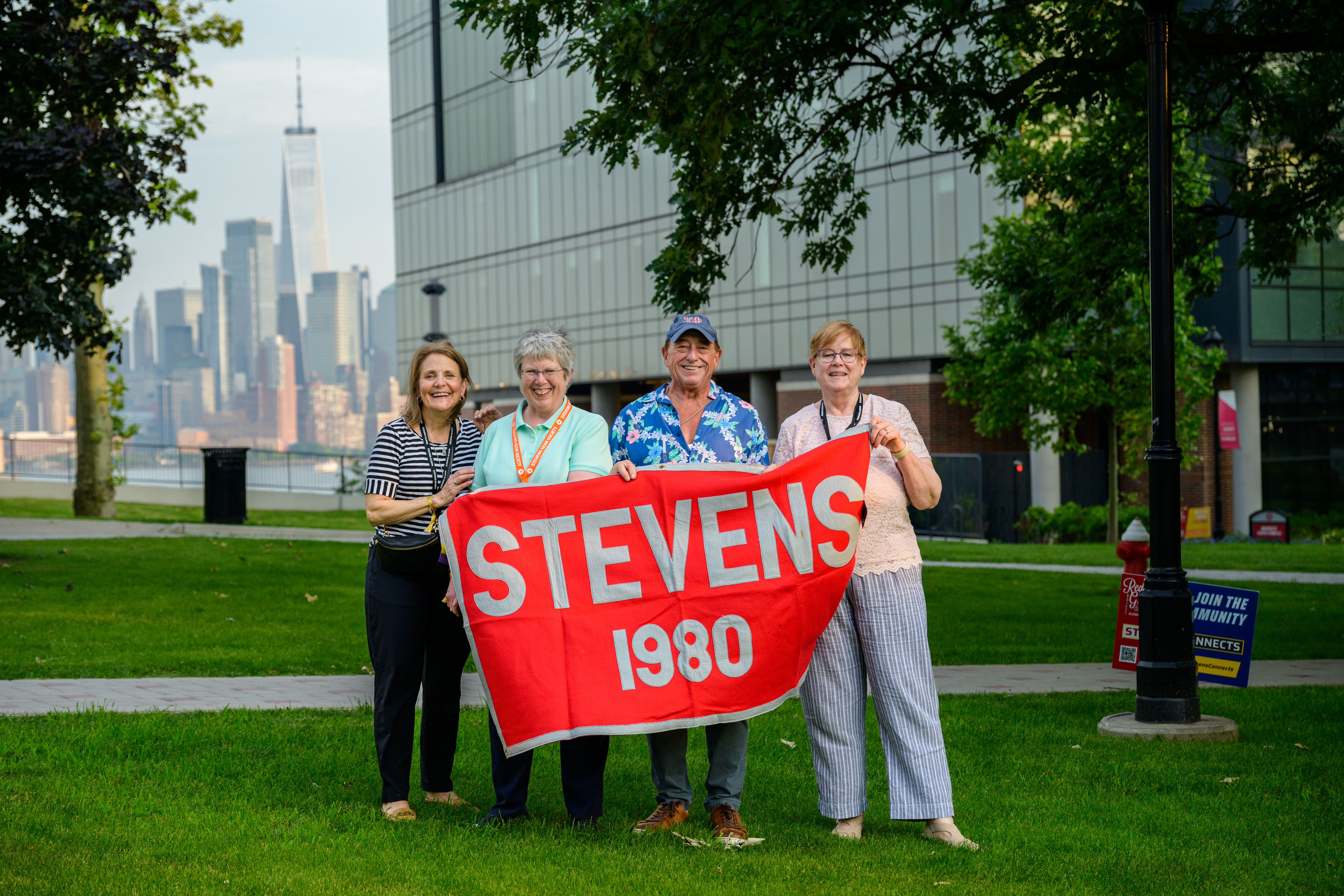 Four alumni hold a Class of 1980 banner at Alumni Weekend 2025 in front of the UCC 