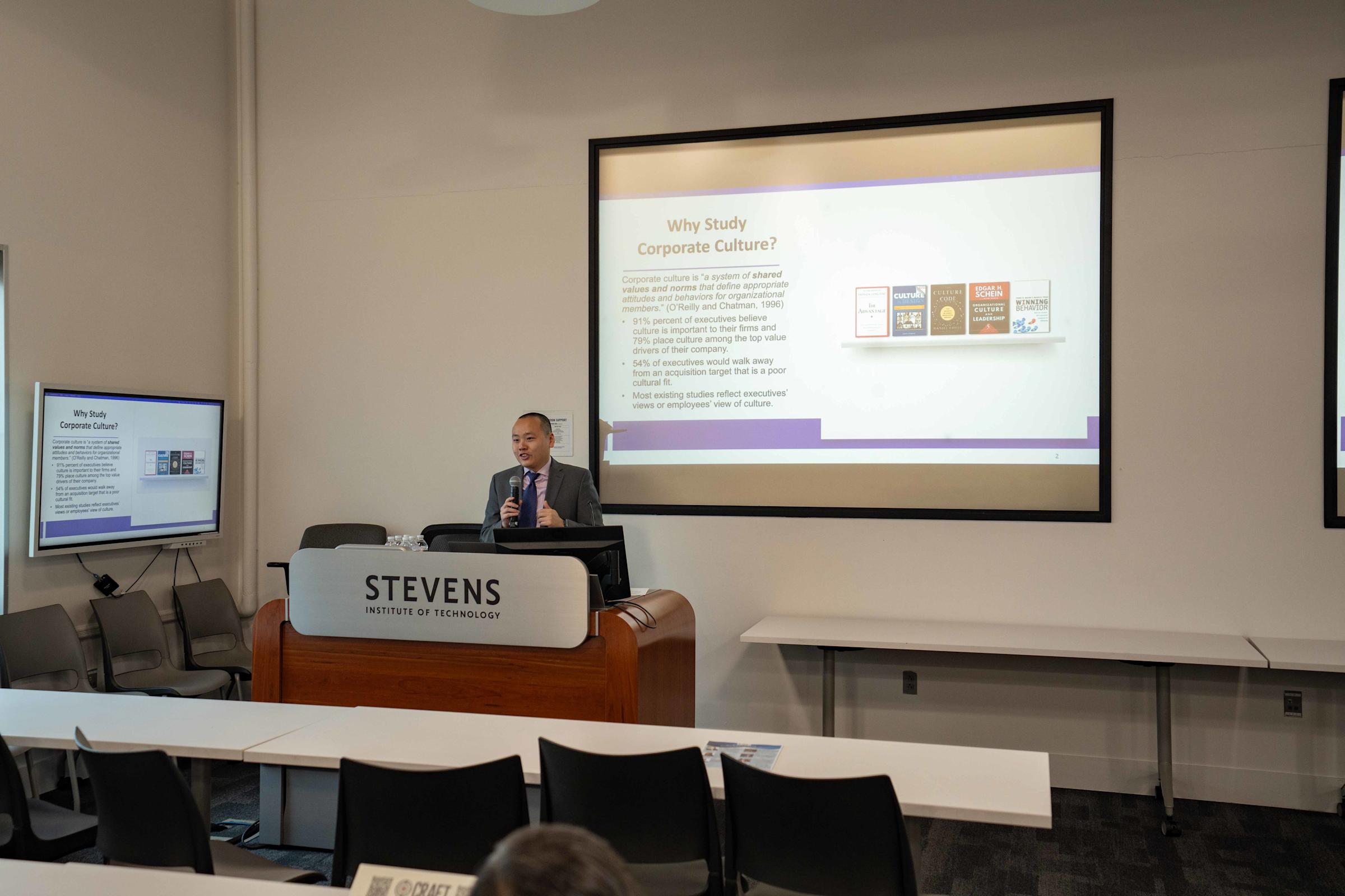 Professor Feng Mai stands in front of a large screen presenting on the topic of “Dissecting Corporate Culture Using Generative AI Insights from Analyst Reports”